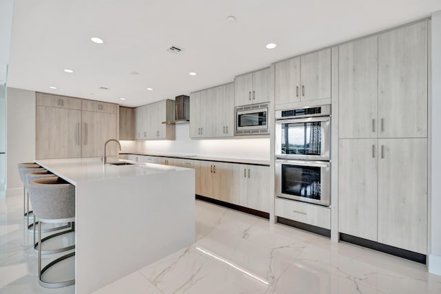 kitchen featuring appliances with stainless steel finishes, a breakfast bar, light brown cabinets, sink, and wall chimney range hood