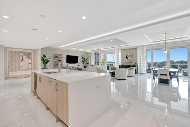 kitchen with hanging light fixtures, sink, a large island, a tray ceiling, and light brown cabinets