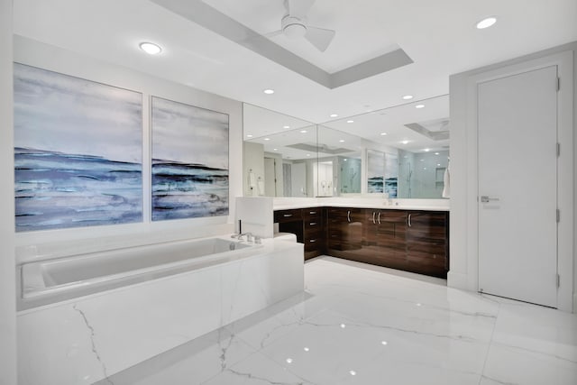 bathroom featuring vanity, tiled tub, ceiling fan, and a tray ceiling