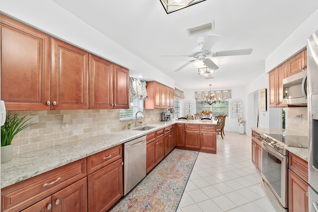 kitchen with sink, tasteful backsplash, pendant lighting, ceiling fan with notable chandelier, and appliances with stainless steel finishes