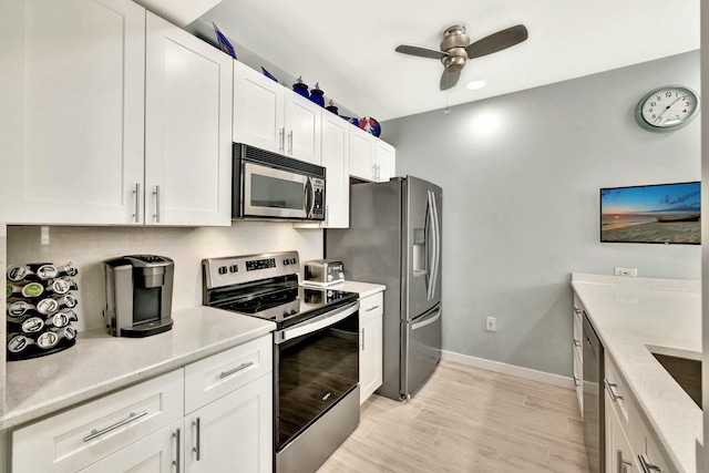 kitchen with white cabinets, ceiling fan, light wood-type flooring, light stone countertops, and stainless steel appliances