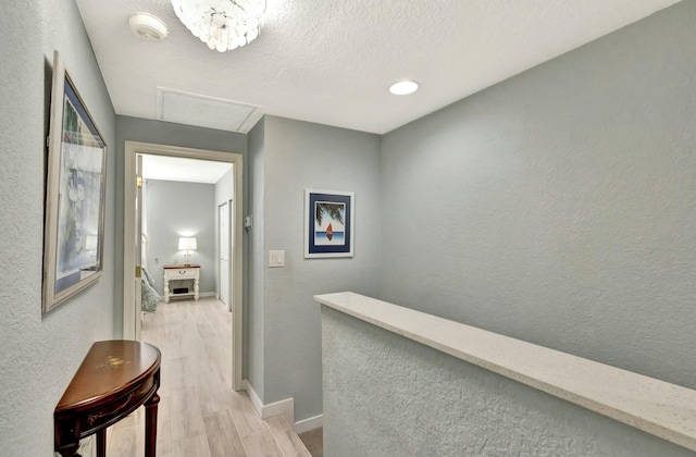 hall featuring an inviting chandelier, a textured ceiling, and light hardwood / wood-style flooring