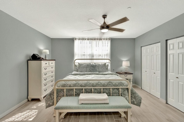 bedroom with multiple closets, ceiling fan, light hardwood / wood-style flooring, and a textured ceiling