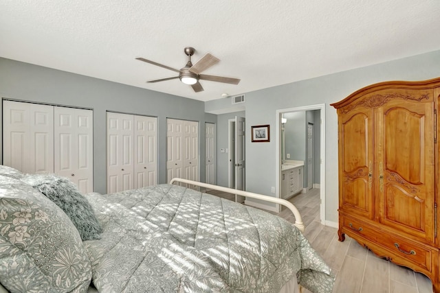 bedroom with light wood-type flooring, ensuite bath, a textured ceiling, two closets, and ceiling fan