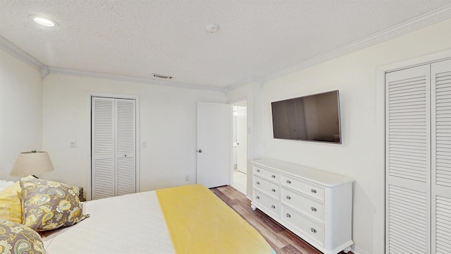 bedroom featuring a textured ceiling, multiple closets, ornamental molding, and wood-type flooring