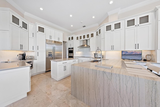 kitchen with sink, a center island with sink, stainless steel appliances, light stone countertops, and wall chimney range hood