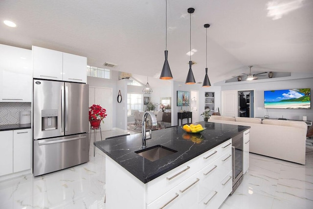 kitchen featuring sink, decorative light fixtures, a center island with sink, stainless steel fridge, and white cabinets