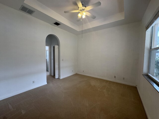 unfurnished room featuring a tray ceiling, ceiling fan, and carpet