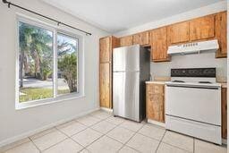 kitchen with light tile patterned floors, white electric range oven, and stainless steel refrigerator