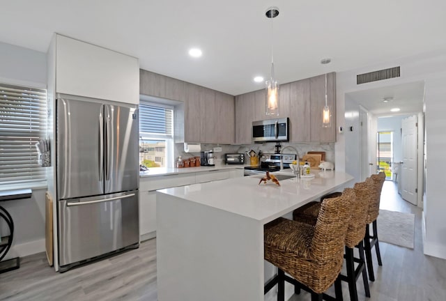 kitchen with stainless steel appliances, pendant lighting, light hardwood / wood-style floors, a breakfast bar area, and decorative backsplash