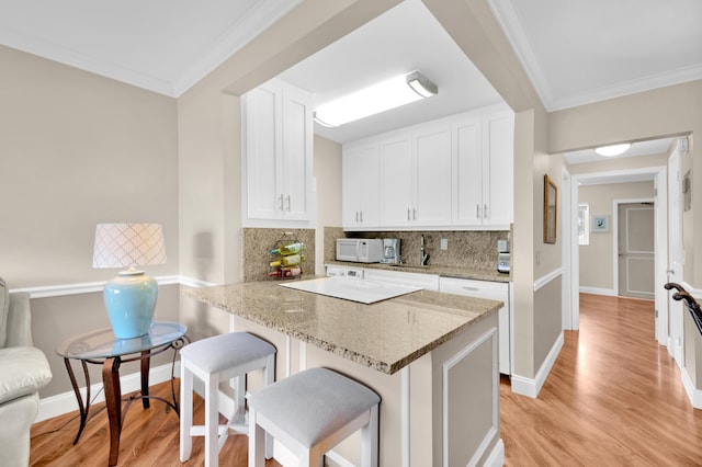 kitchen with kitchen peninsula, decorative backsplash, light stone counters, white cabinetry, and a breakfast bar area