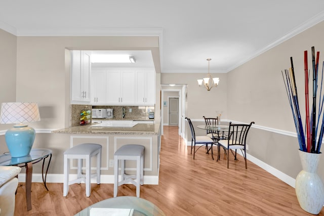 kitchen featuring a notable chandelier, kitchen peninsula, pendant lighting, decorative backsplash, and white cabinets