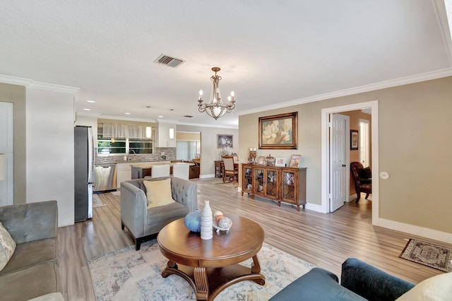 living room featuring crown molding, light hardwood / wood-style flooring, sink, and a notable chandelier