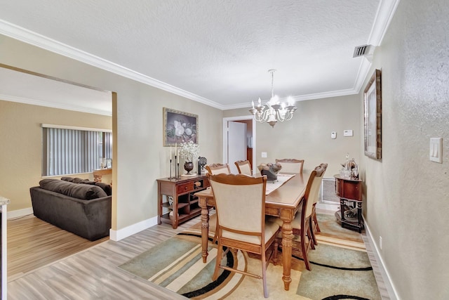 dining area featuring light hardwood / wood-style flooring, a chandelier, a textured ceiling, and ornamental molding