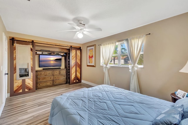 bedroom featuring a barn door, light hardwood / wood-style floors, and ceiling fan