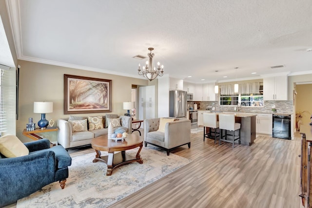 living room with light hardwood / wood-style floors, crown molding, beverage cooler, and an inviting chandelier