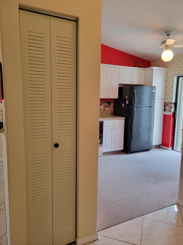 kitchen featuring light carpet, white cabinetry, black refrigerator, lofted ceiling, and a textured ceiling