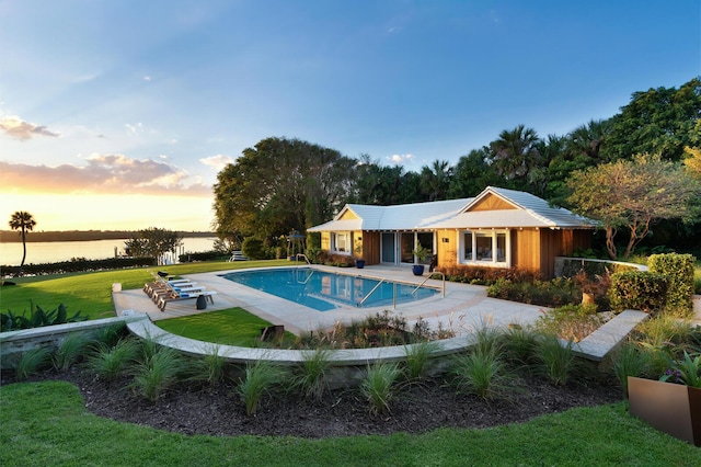 pool at dusk with a water view, a yard, an outdoor structure, and a patio