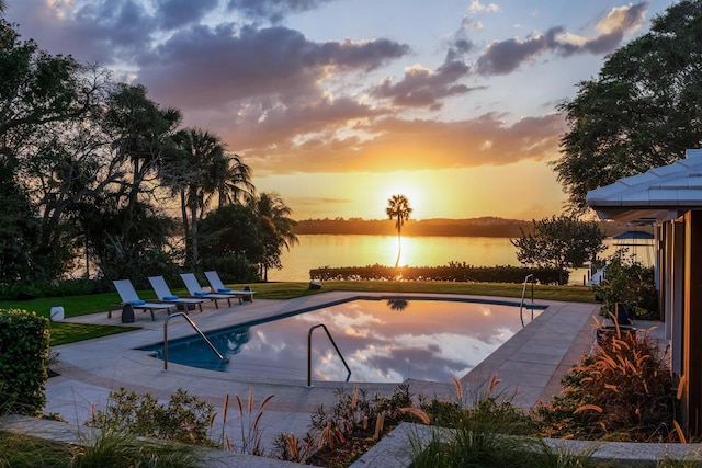 pool at dusk featuring a water view and a patio area