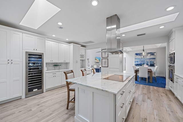 kitchen featuring a breakfast bar, island exhaust hood, a kitchen island, wine cooler, and white cabinetry