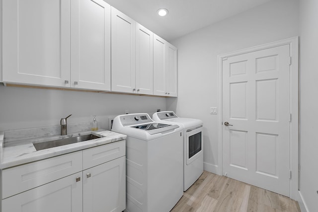 laundry room featuring independent washer and dryer, cabinets, light hardwood / wood-style floors, and sink