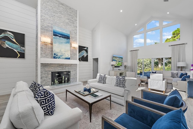 living room featuring hardwood / wood-style flooring, high vaulted ceiling, wooden walls, and a stone fireplace