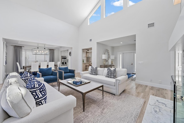 living room with a healthy amount of sunlight, light hardwood / wood-style flooring, an inviting chandelier, and high vaulted ceiling