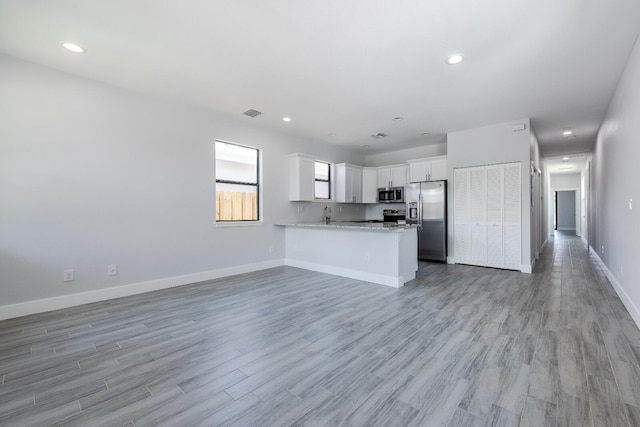 kitchen featuring open floor plan, light wood-type flooring, appliances with stainless steel finishes, a peninsula, and white cabinets