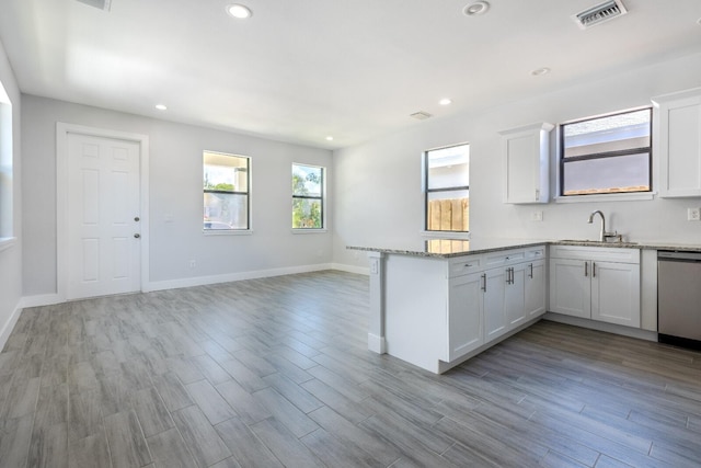 kitchen featuring kitchen peninsula, light stone countertops, stainless steel dishwasher, sink, and white cabinets