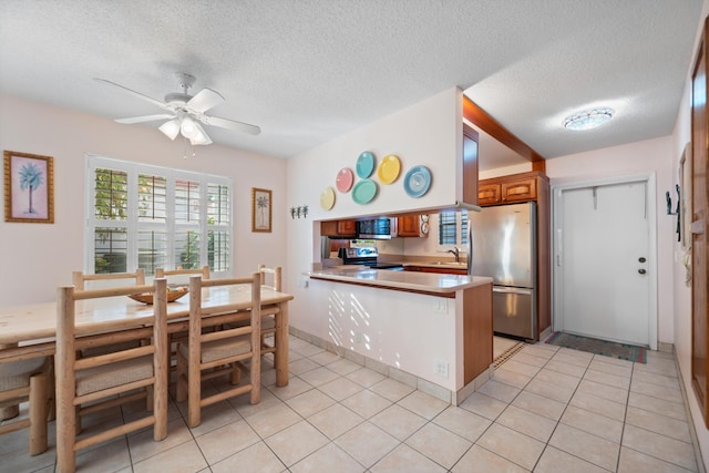 kitchen with stainless steel appliances, kitchen peninsula, a textured ceiling, and light tile patterned floors