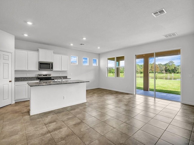 kitchen with appliances with stainless steel finishes, light tile patterned floors, a center island with sink, dark stone countertops, and white cabinetry