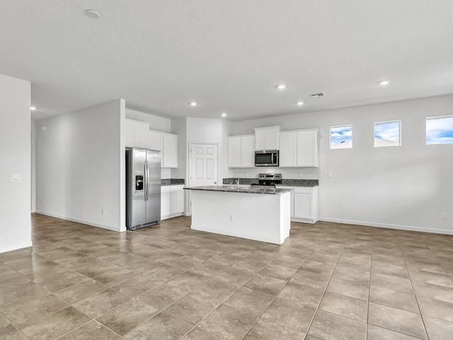 kitchen with white cabinetry, stainless steel appliances, a center island with sink, and dark stone countertops