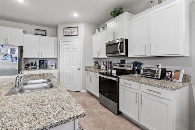 kitchen featuring sink, white cabinetry, a textured ceiling, stainless steel appliances, and light stone countertops