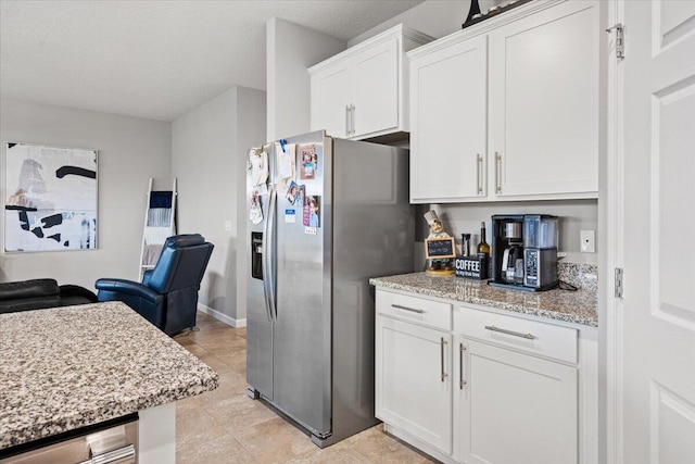 kitchen featuring a textured ceiling, stainless steel fridge, light stone countertops, and white cabinets