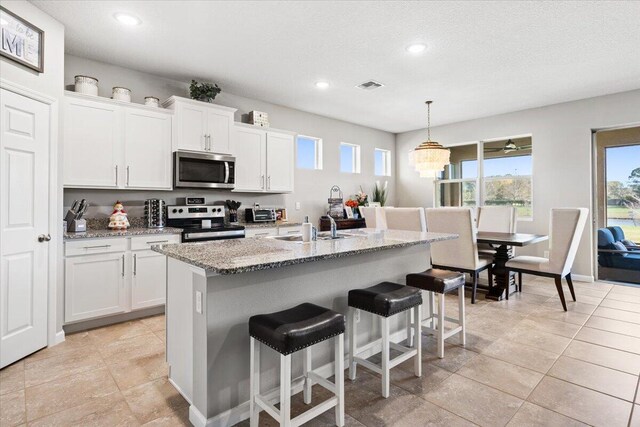 kitchen featuring appliances with stainless steel finishes, a center island with sink, white cabinets, and decorative light fixtures