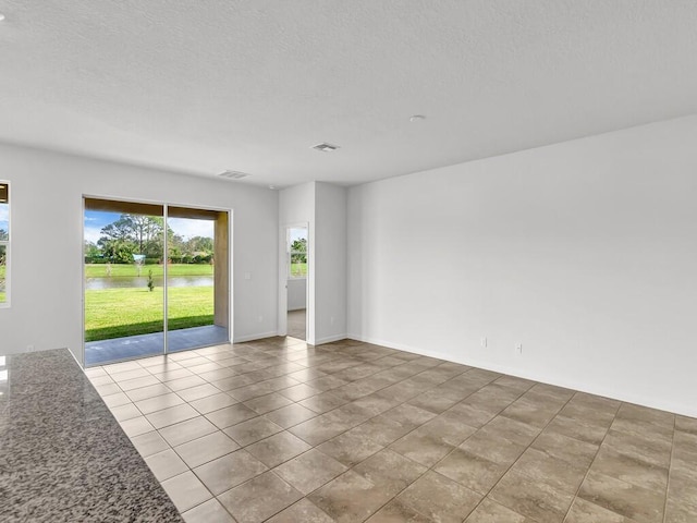 empty room featuring a water view, a textured ceiling, and light tile patterned floors