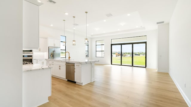 kitchen featuring a center island with sink, a raised ceiling, white cabinetry, and appliances with stainless steel finishes