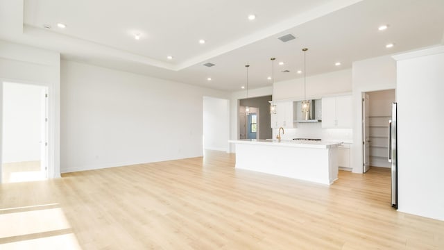 unfurnished living room featuring a raised ceiling and light hardwood / wood-style floors