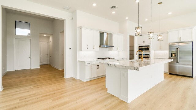 kitchen featuring white cabinetry, a kitchen island with sink, wall chimney range hood, and appliances with stainless steel finishes