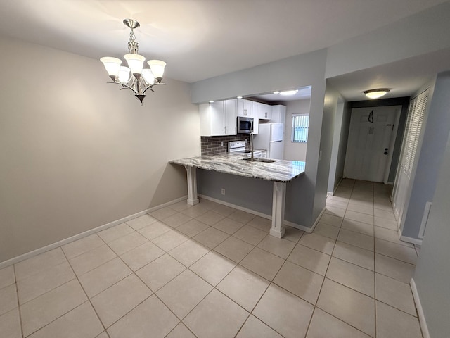 kitchen featuring white appliances, white cabinetry, light stone counters, decorative light fixtures, and kitchen peninsula