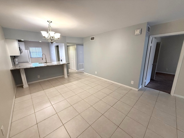 kitchen featuring sink, white cabinets, hanging light fixtures, light stone counters, and kitchen peninsula