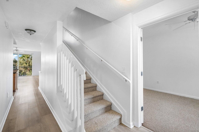 stairway with hardwood / wood-style floors, a textured ceiling, and ceiling fan