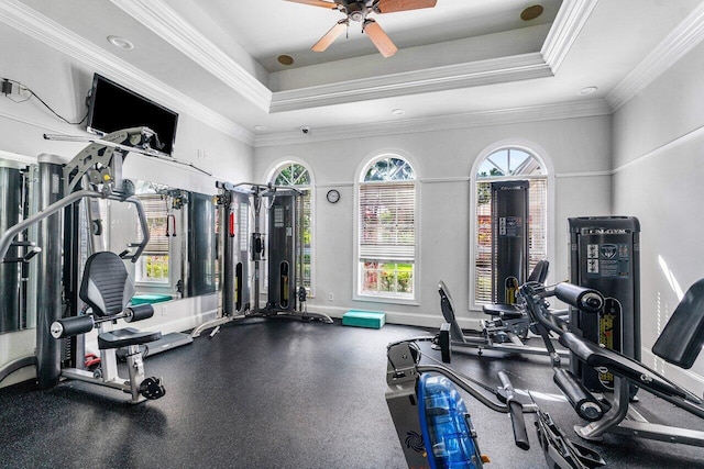 gym featuring a raised ceiling, ceiling fan, and ornamental molding