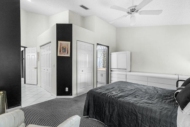 bedroom featuring ceiling fan, a high ceiling, a textured ceiling, light tile patterned floors, and two closets