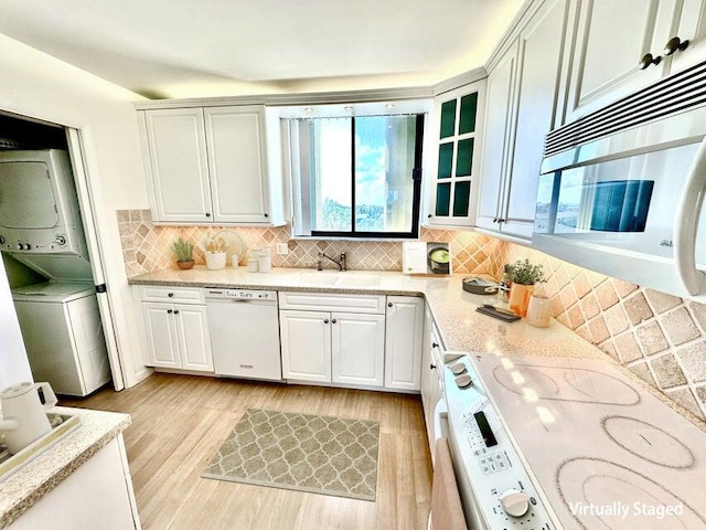 kitchen with white appliances, white cabinets, stacked washer and clothes dryer, and sink