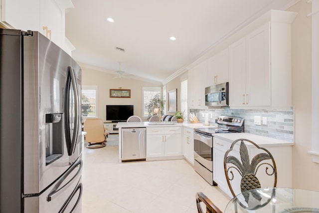 kitchen with stainless steel appliances, tasteful backsplash, kitchen peninsula, vaulted ceiling, and white cabinets