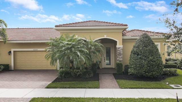 mediterranean / spanish-style home featuring an attached garage, a tile roof, decorative driveway, and stucco siding