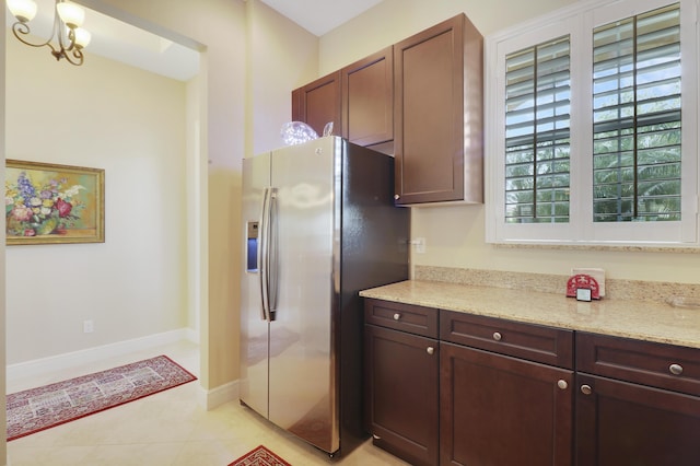 kitchen with light stone counters, light tile patterned flooring, a notable chandelier, baseboards, and stainless steel refrigerator with ice dispenser