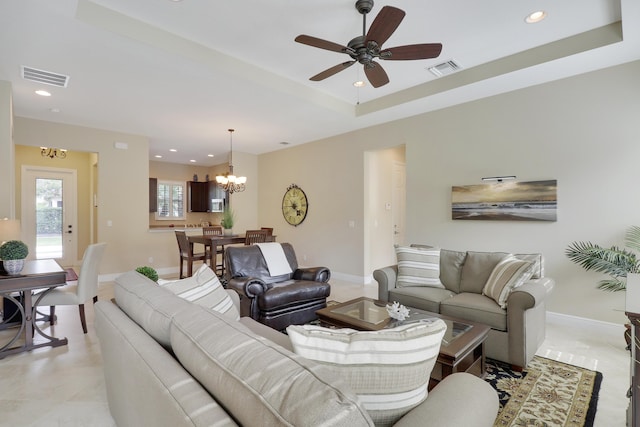 living room with light tile patterned floors, ceiling fan with notable chandelier, and a raised ceiling