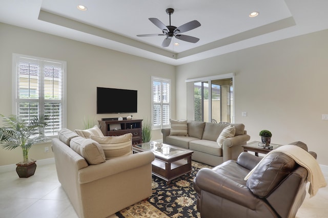 tiled living room with ceiling fan and a raised ceiling